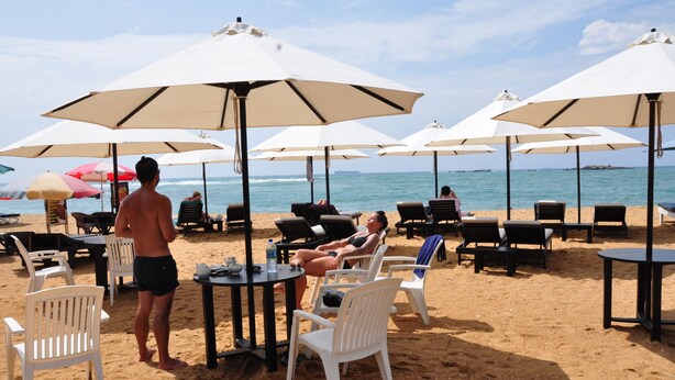 Un entorno de playa con sillas, mesas y sombrillas blancas.