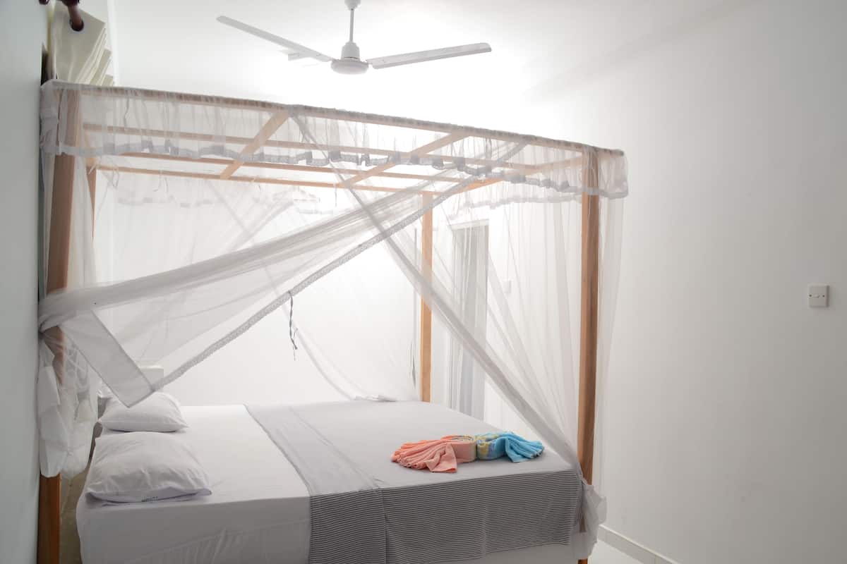 Una cama con dosel, un ventilador de techo y una ventana con cortinas.