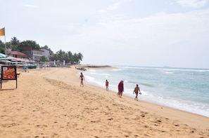 A beach with people walking along the shore, a sign for a pizza restaurant, and buildings in the background. - SURF UNA Beach Hotel (Unawatuna)