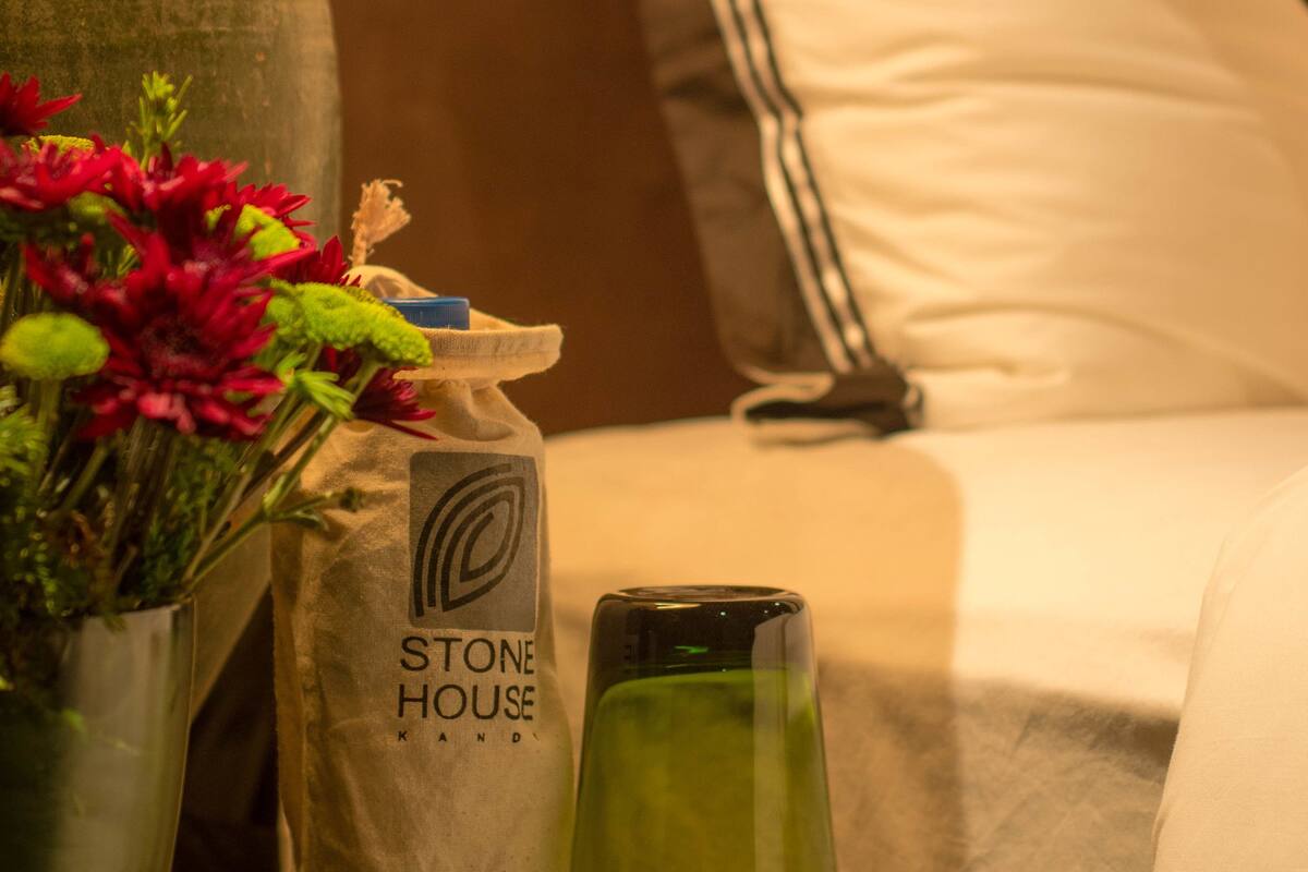 Una mesita de noche ordenada con un jarrón de flores, una bolsa de marca y un recipiente de vidrio.