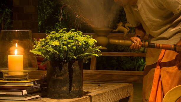 Una mesa iluminada con velas, una planta en maceta, un libro y una persona vestida con traje tradicional.