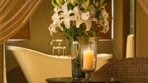 Un baño con una bañera, un florero con flores y una vela sobre una mesa.