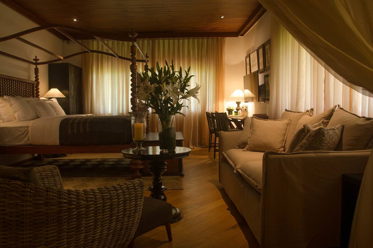 Una habitación de hotel con cama, sofá, mesa de comedor y un jarrón de flores.