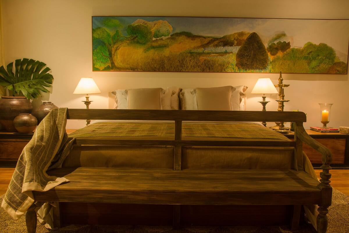 Una cama con cabecera de madera, dos lámparas de noche y un cuadro de un paisaje en la pared.