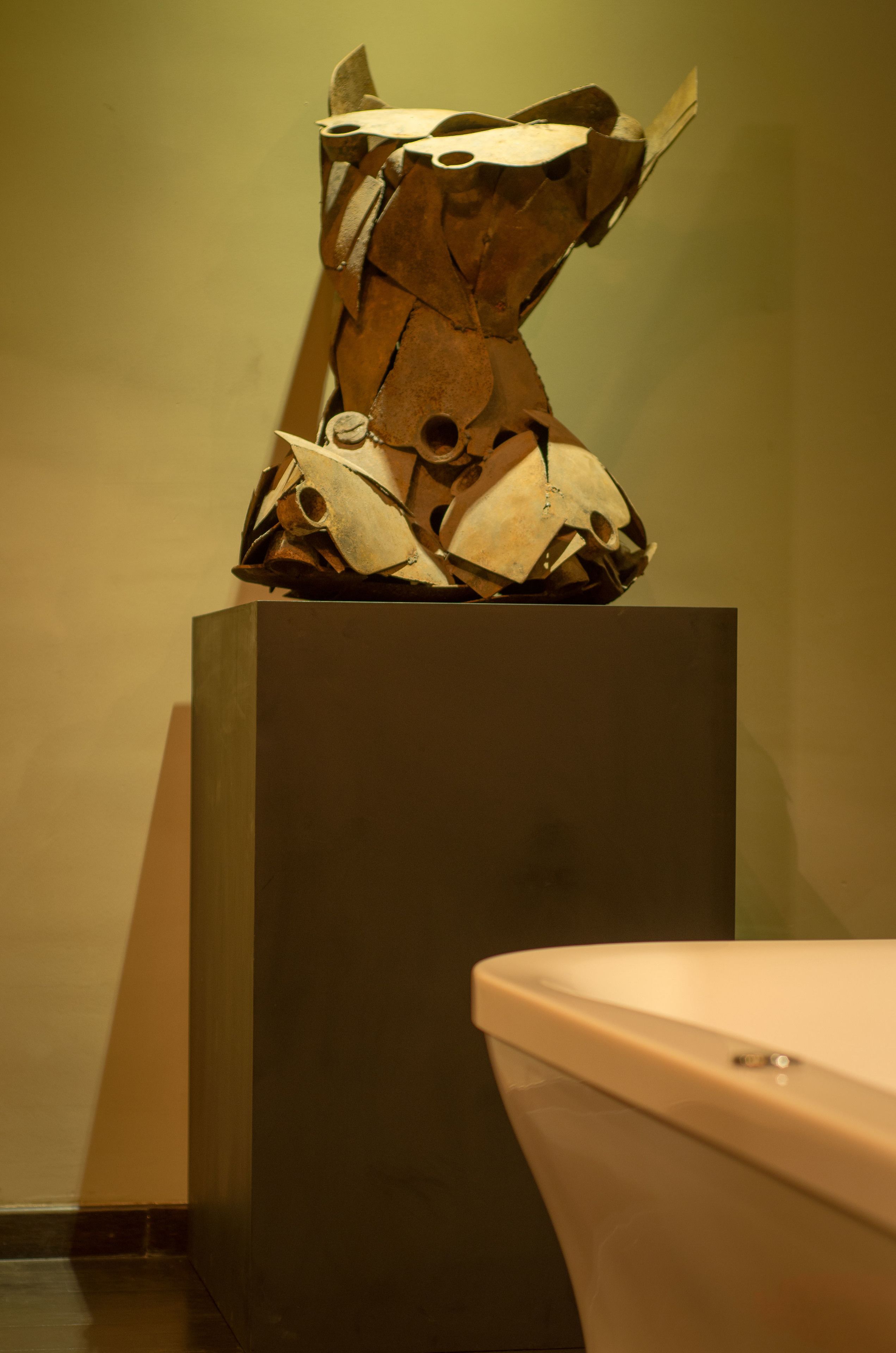 Eine Skulptur auf einem Sockel in einem Raum, im Hintergrund ist eine Toilette erkennbar.