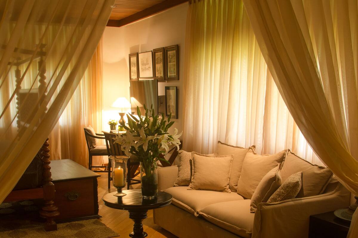 Una sala de estar acogedora con un sofá, un sillón de mimbre, una mesa con un florero y una lámpara.