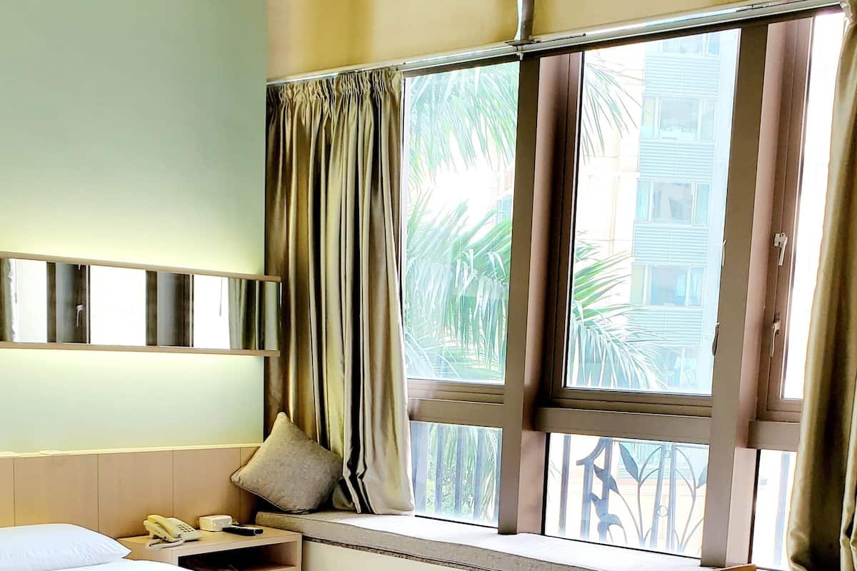 A hotel room with a large bed, a desk, a chair, and a window with curtains.