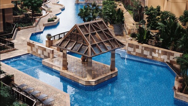 A resort pool area with multiple swimming pools, a central water feature, and surrounding greenery. - Winland 800 Hotel (Tsing Yi)
