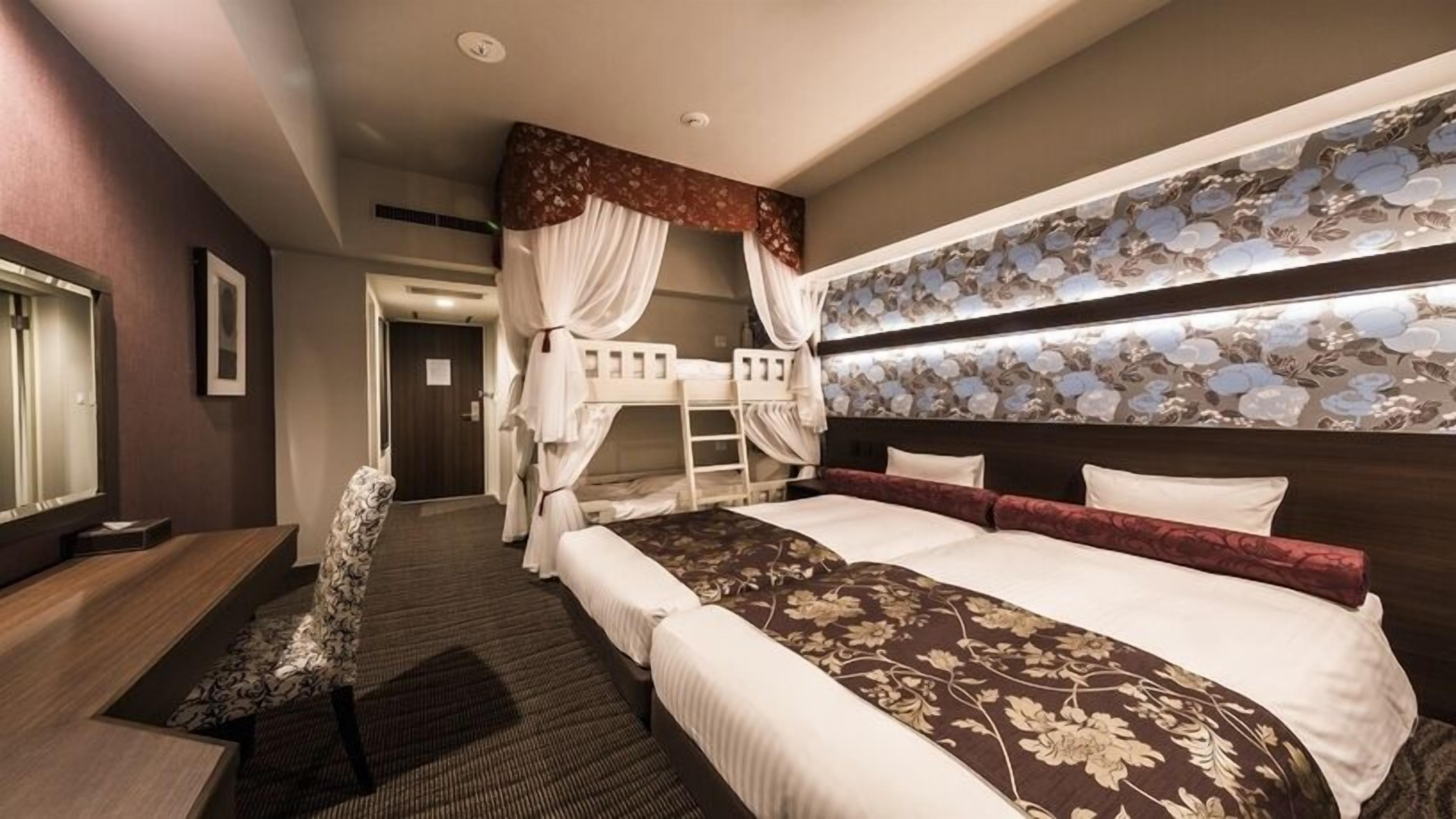 A hotel room with a large bed, a desk, a chair, and a wardrobe.