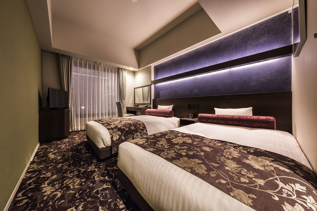 A hotel room with two beds, a large mirror, and a television.
