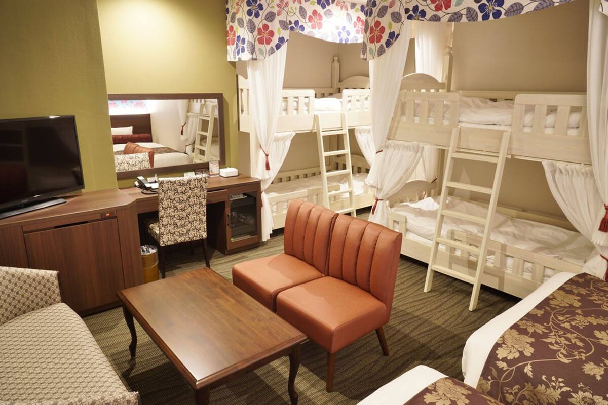 A hotel room with bunk beds, a television, a sofa, a desk, and a mirror.