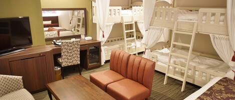 A hotel room with bunk beds, a television, a sofa, a desk, and a mirror.