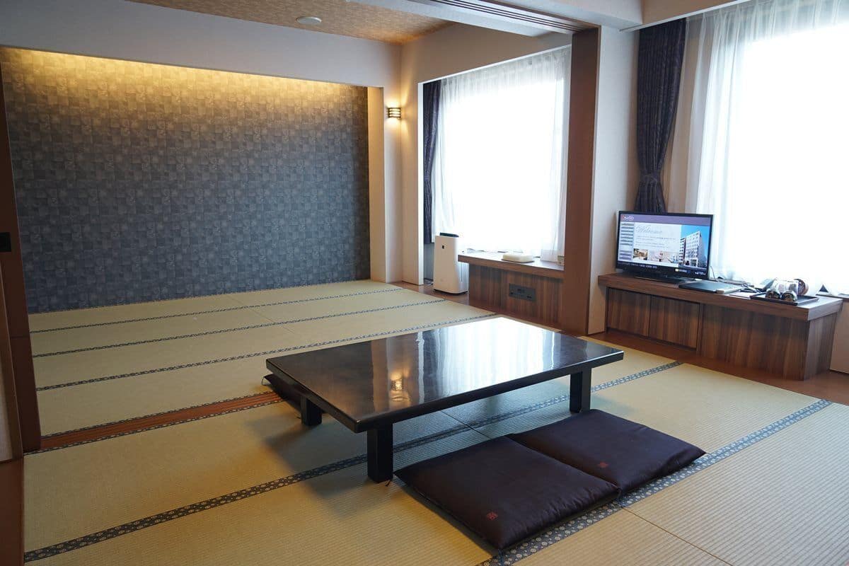 A traditional Japanese room with tatami flooring, a low table, cushions, a television, and a wooden cabinet.