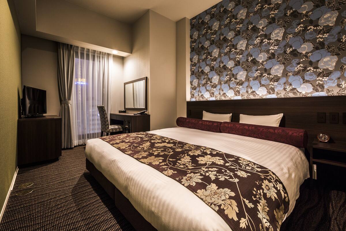 A hotel room with a large bed, a desk, a chair, a TV, and a decorative wall.