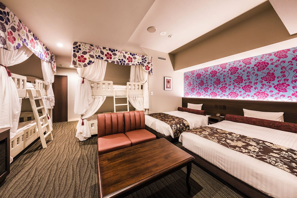 A hotel room with two beds, a sofa, a wooden table, and a decorative canopy.