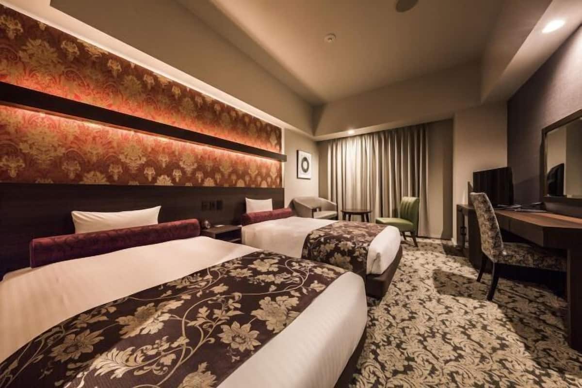 A hotel room with two beds, a desk, a chair, a mirror, and a patterned carpet.