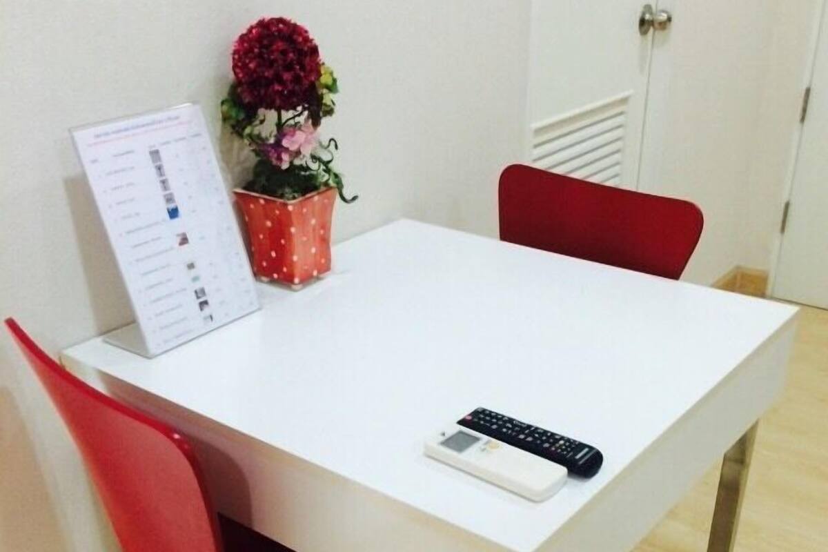 A white table with a remote control, a red chair, and a potted plant with flowers.