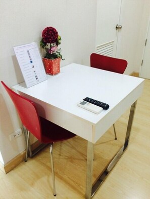 A white table with a remote control, a red chair, and a potted plant with flowers.