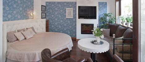 Un dormitorio con una cama grande, televisor, chimenea y zona de comedor con sillas y mesa.