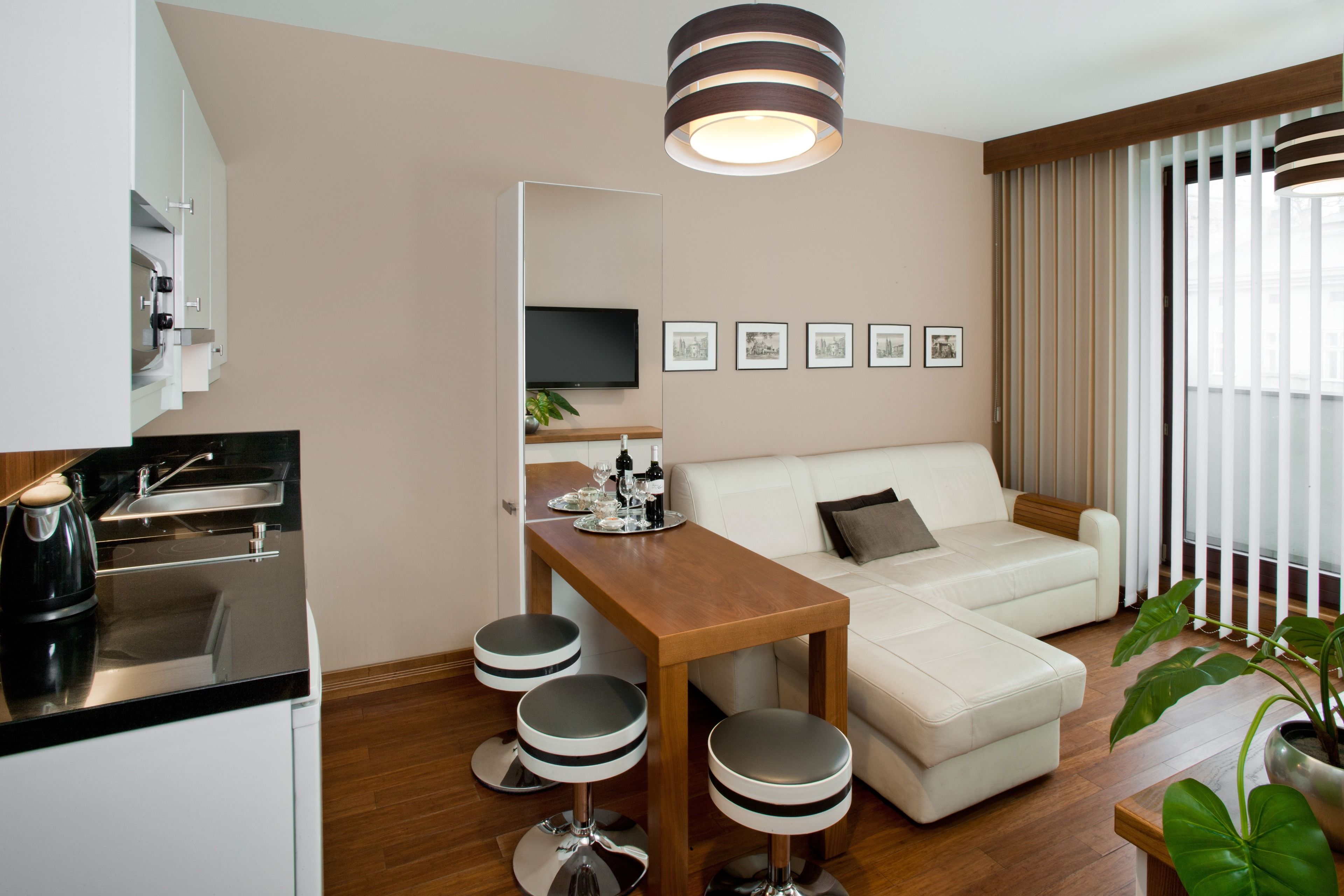 A modern living room with a sofa, a wooden coffee table, and a kitchen area with a kettle and bar stools.