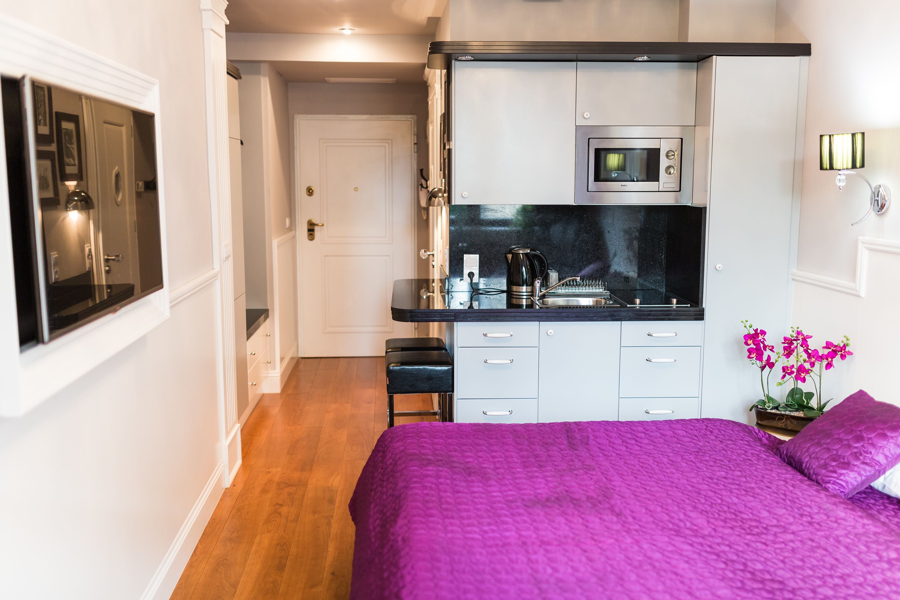 Un dormitorio compacto con cama, una kitchenette pequeña y una puerta que da a otra habitación.