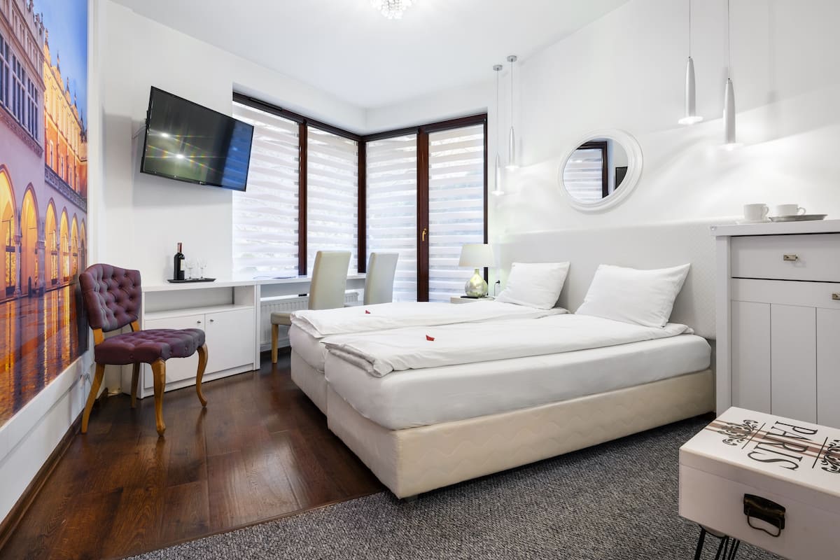 Ett modernt hotellrum med en stor säng, ett skrivbord, en stol, en TV och ett stort fönster med persienner.