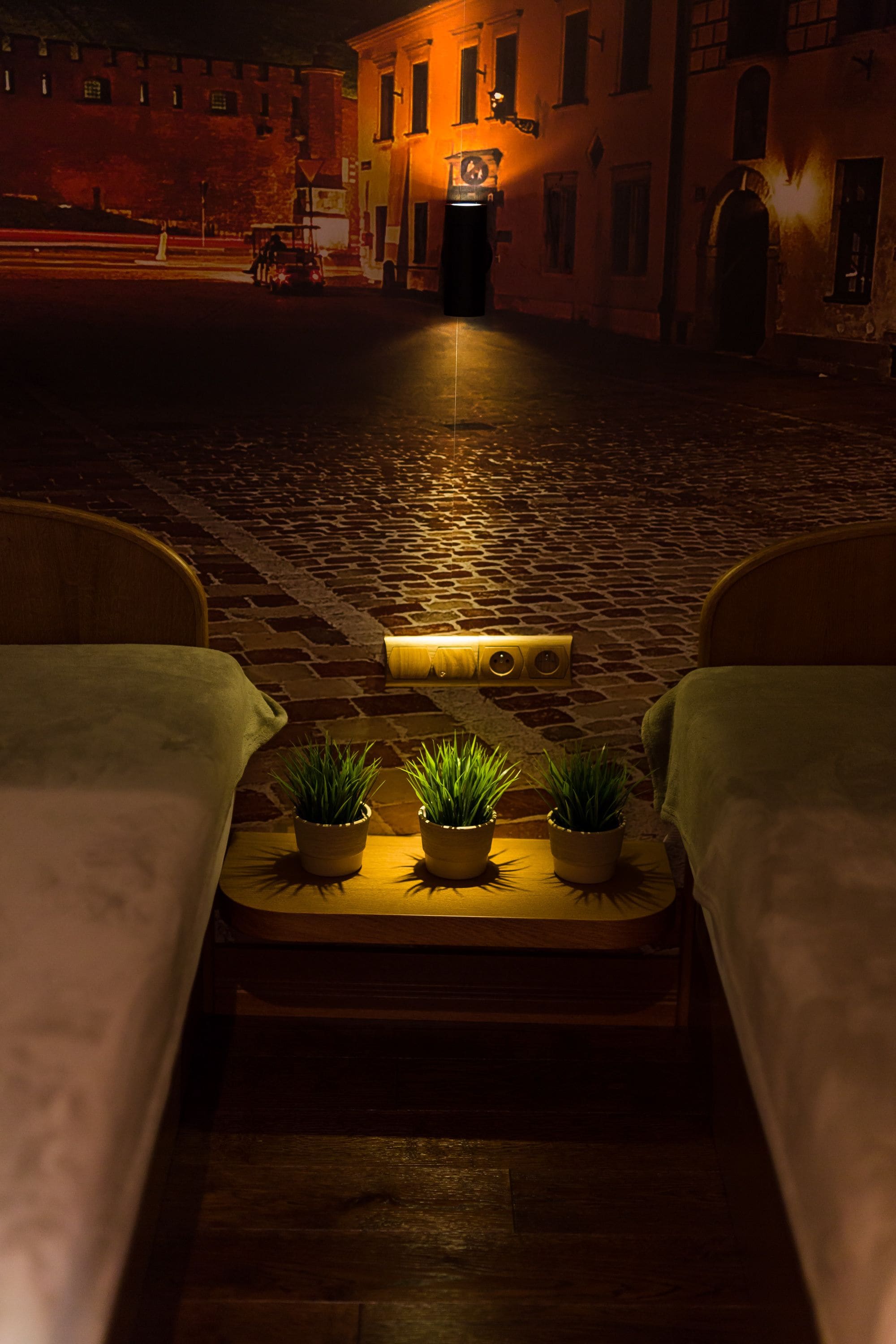 A cozy bed with a small table and potted plants in the center of a cobblestone street at night.