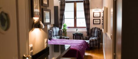 A hotel room with a bed, two armchairs, a small table, and a window with curtains.