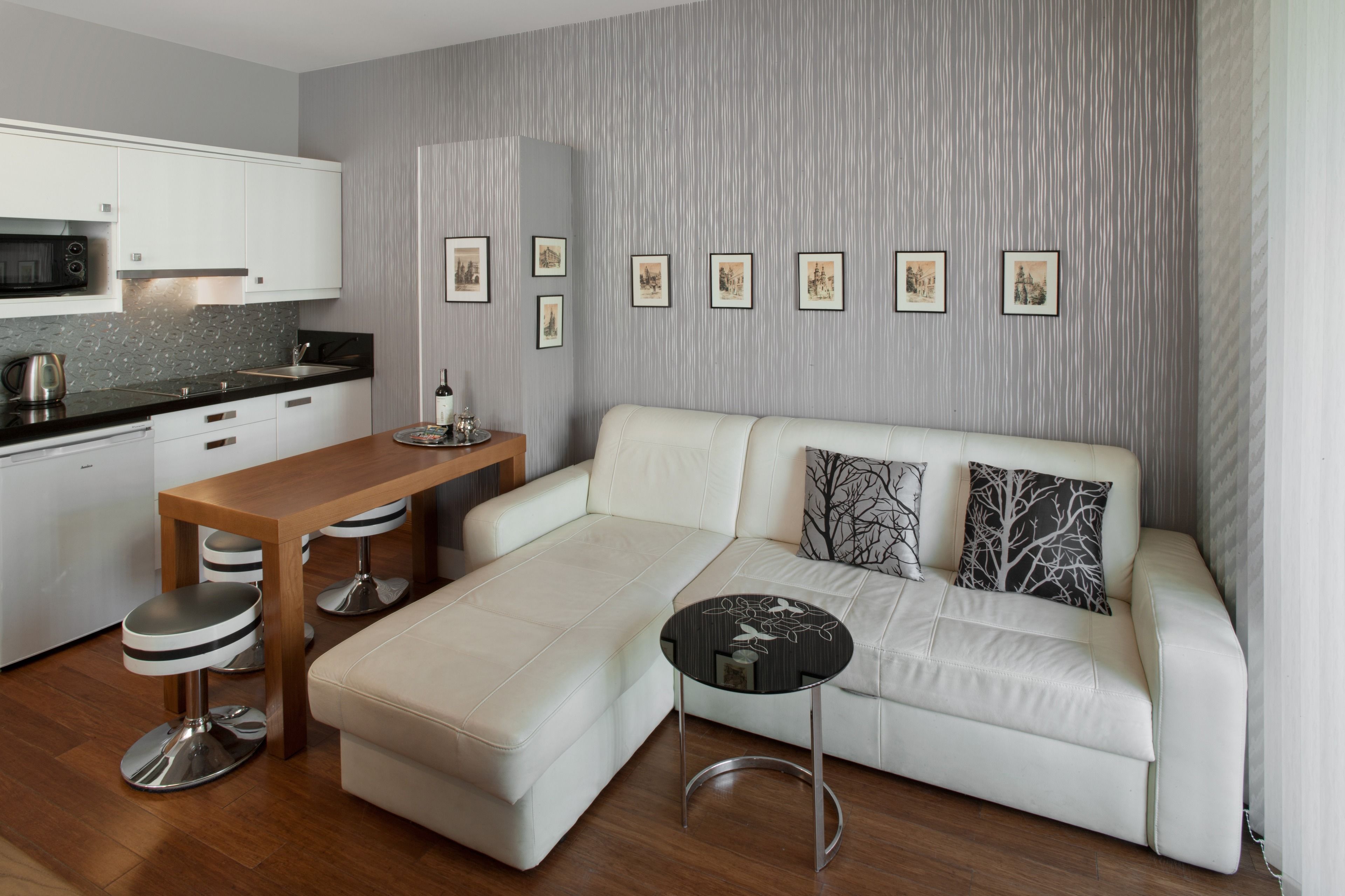 A modern living room with a white sofa, a wooden coffee table, and a kitchen area with white cabinets and a microwave.