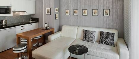A modern living room with a white sofa, a wooden coffee table, and a kitchen area with white cabinets and a microwave.