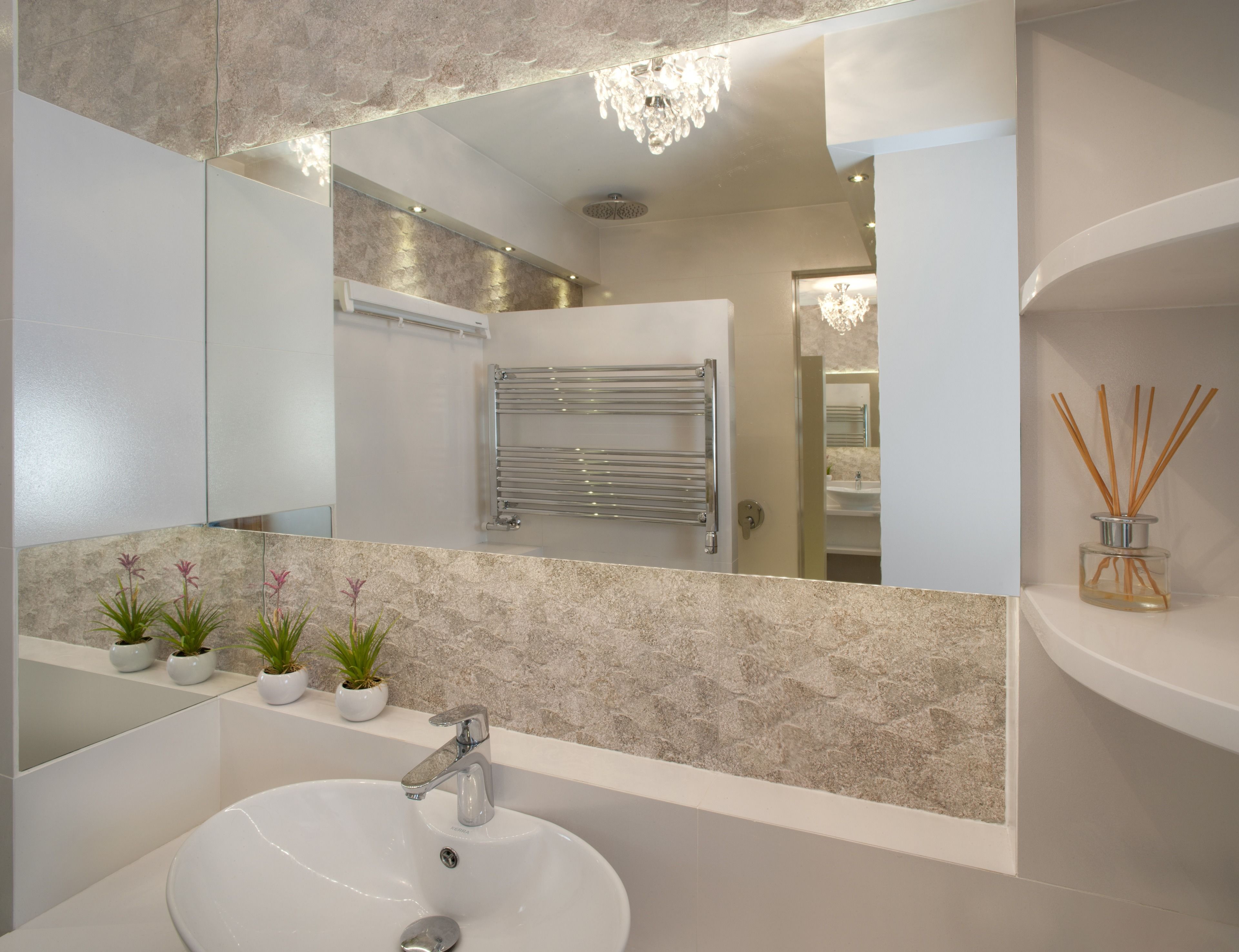 A modern bathroom with a large mirror, a white sink, and a towel rack.