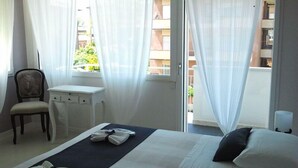 A hotel room with a bed, a desk, a chair, and a window with sheer curtains. - Villa Venice Movie (Venice)