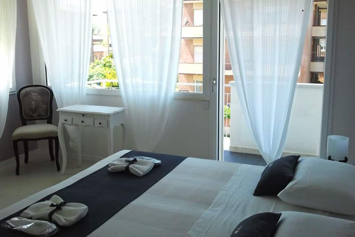 A hotel room with a bed, a desk, a chair, and a window with sheer curtains.