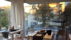 A dining area with a table and chairs, a basket of bread, and a window with a view of the street and buildings. - Villa Venice Movie (Venice)