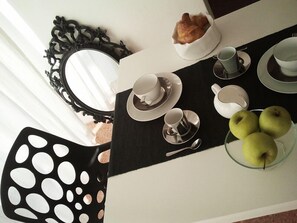 A dining area with a table set for two, including plates, cups, a teapot, and a bowl of apples.