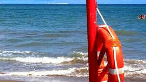 A lifebuoy attached to a pole on a sandy beach with the ocean in the background. - Villa Venice Movie (Venice)