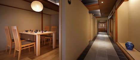 A hallway with a dining area featuring a wooden table and chairs, a hanging light fixture, and a tiled floor.