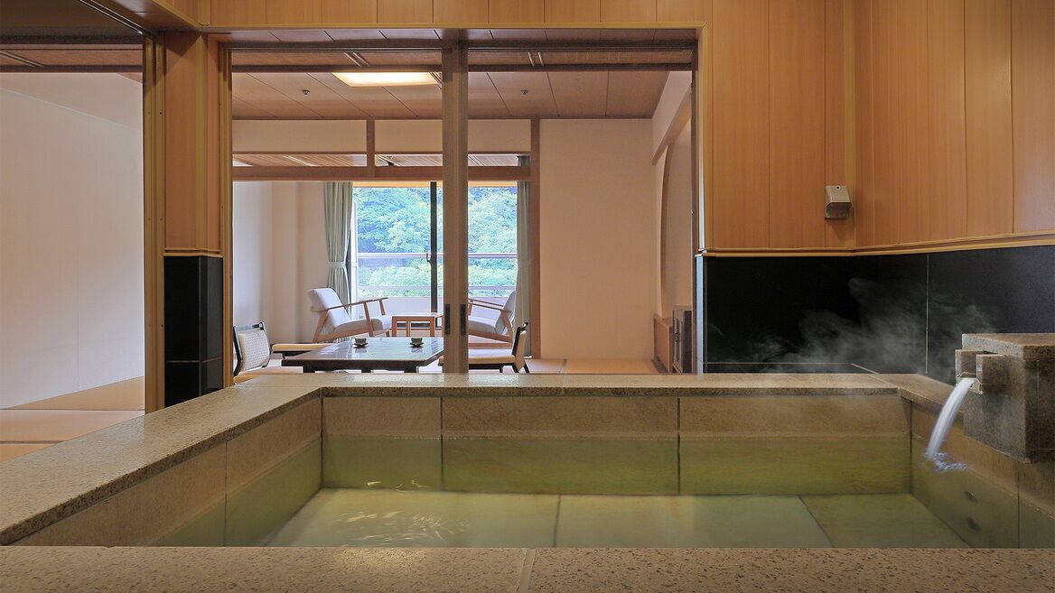 A hot spring bath area with a stone bench, wooden walls, and a view of the outdoors.