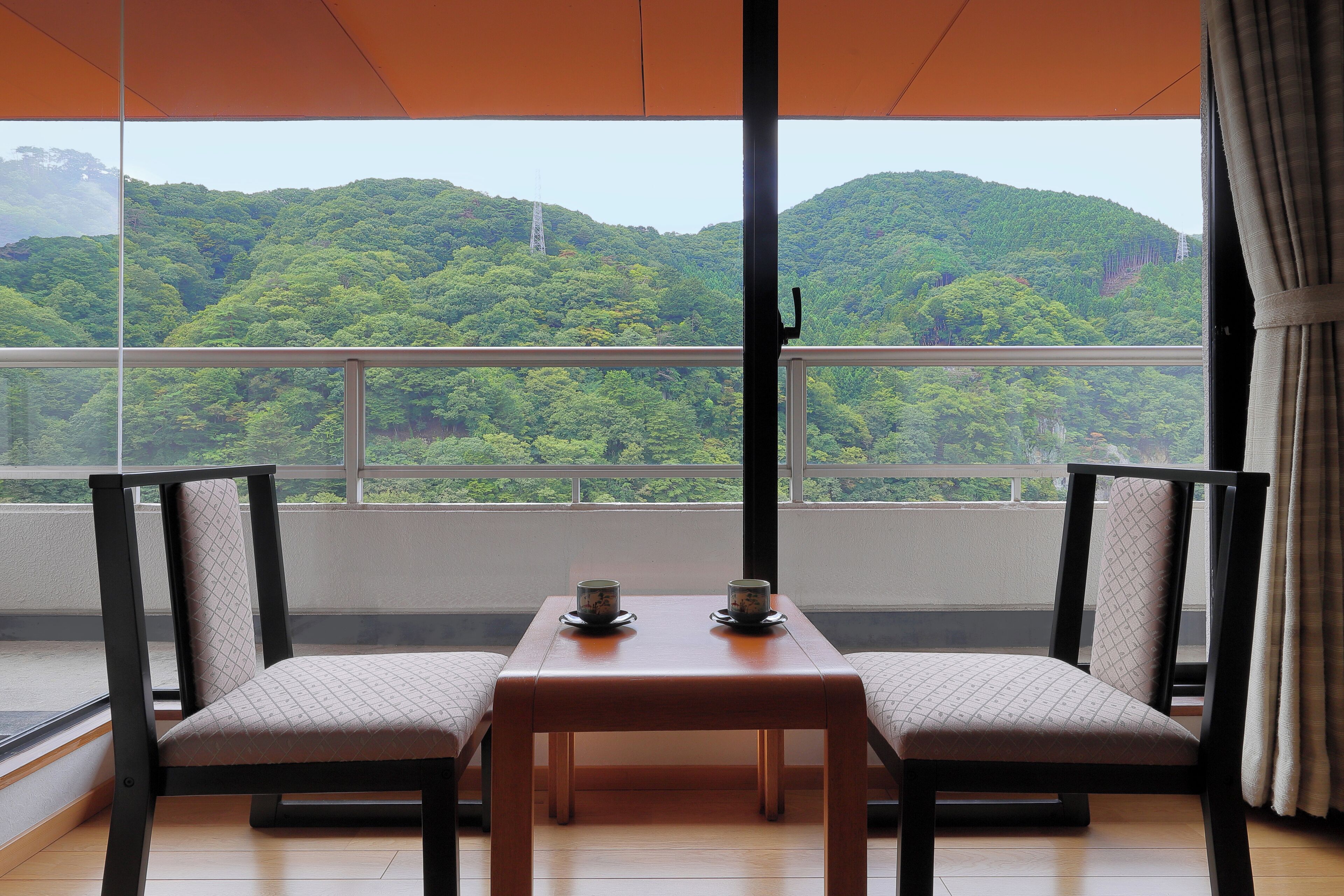 A balcony with two chairs and a table, overlooking a lush green hillside.