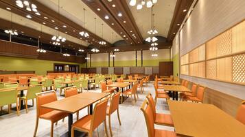 A spacious dining area with multiple tables and chairs, high ceilings with hanging lights, and a large window with a lattice design.