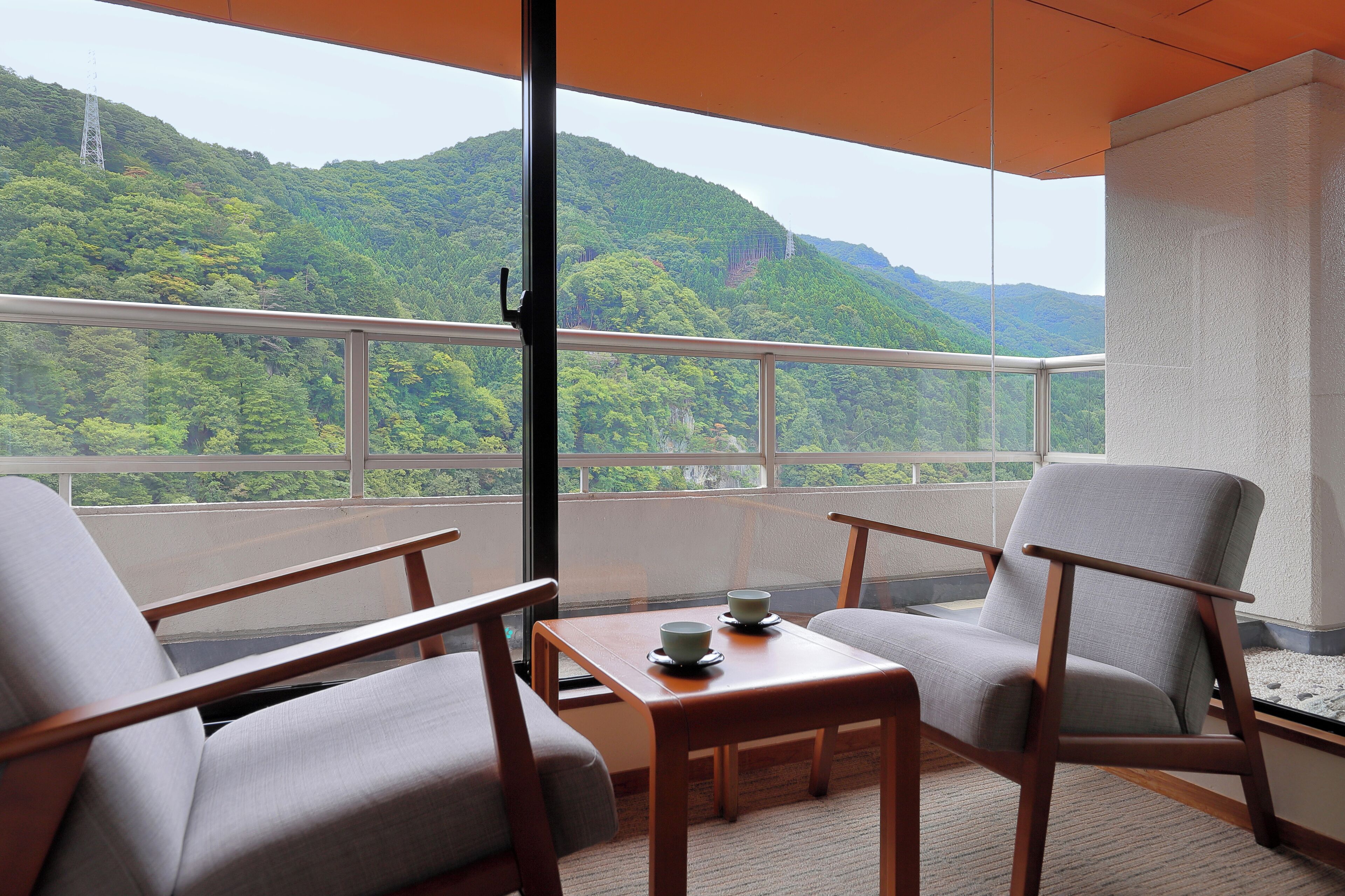 Un balcón con dos sillas y una mesa, con vistas a un paisaje montañoso exuberante y verde.