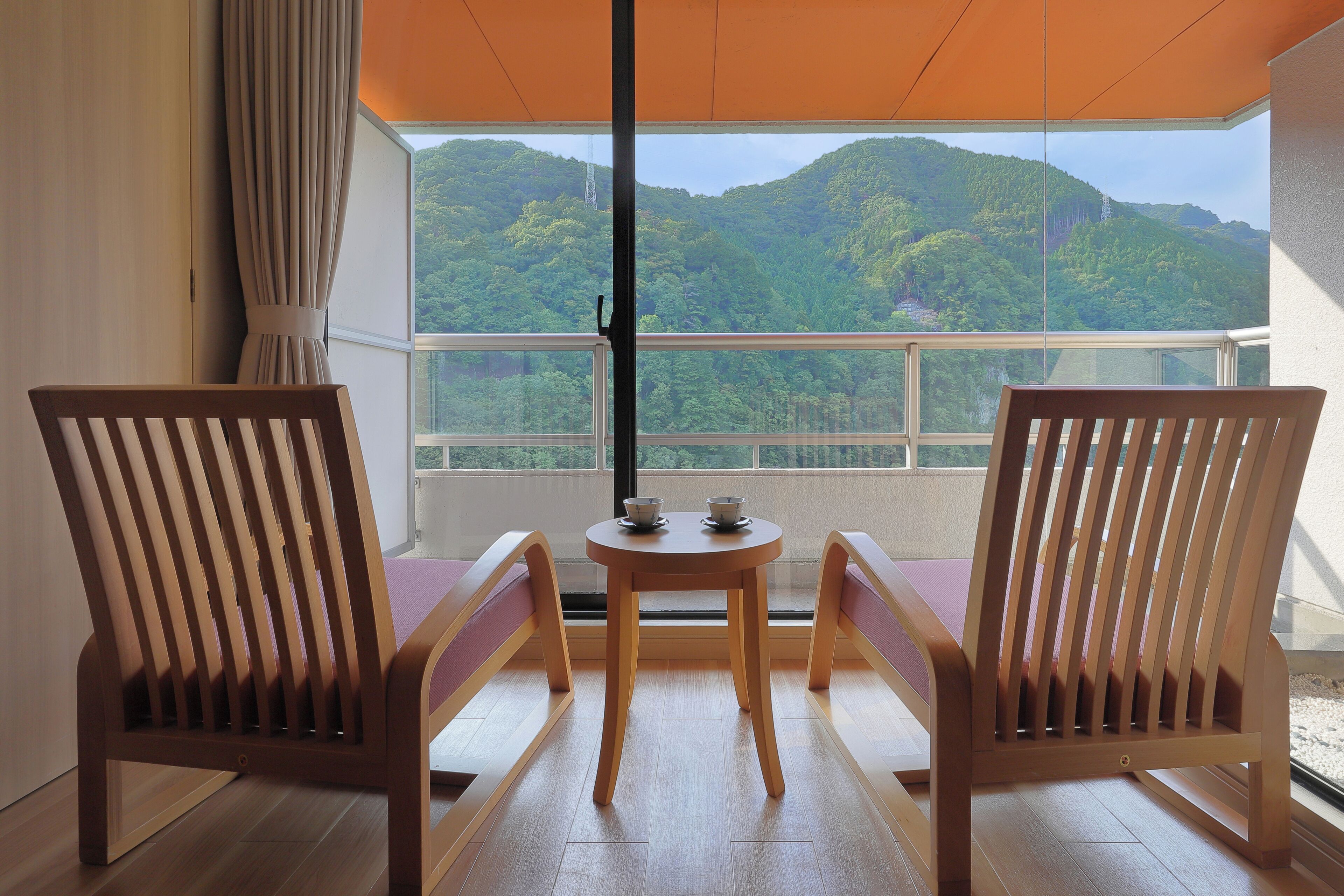 A balcony with two wooden chairs and a small table, overlooking a mountainous landscape.