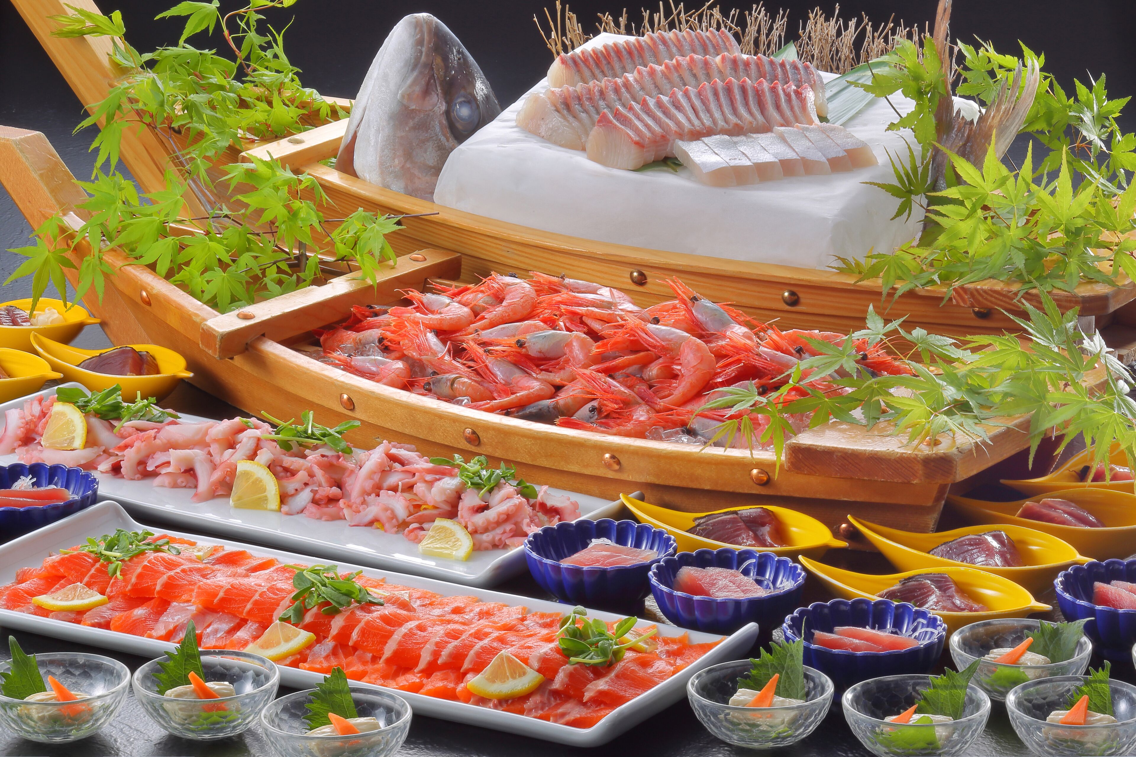 A variety of seafood arranged on a table, including shrimp, salmon, and other fish, with small bowls and plates.