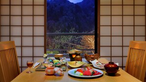 Una comida tradicional japonesa con varios platos y una vela, vista a través de una ventana con vistas a montañas.