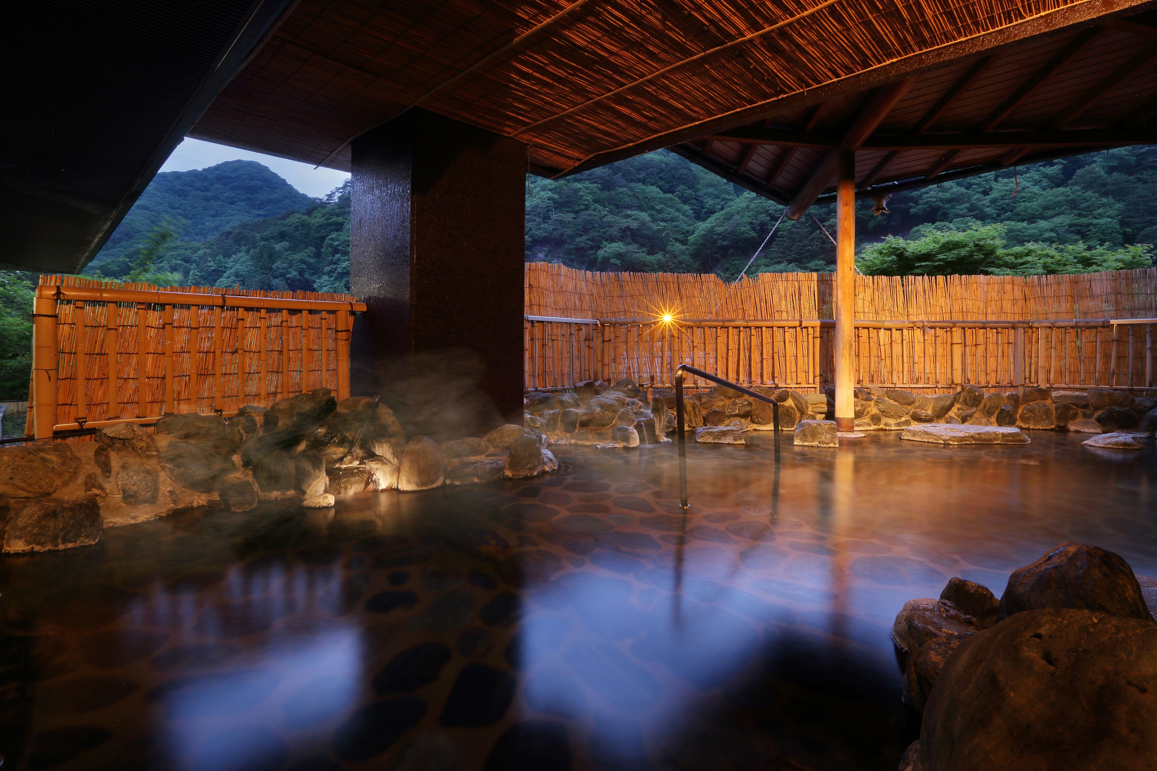 Un área de baño de aguas termales tradicional con suelo de piedra, paredes de bambú y estructura de techo de madera.
