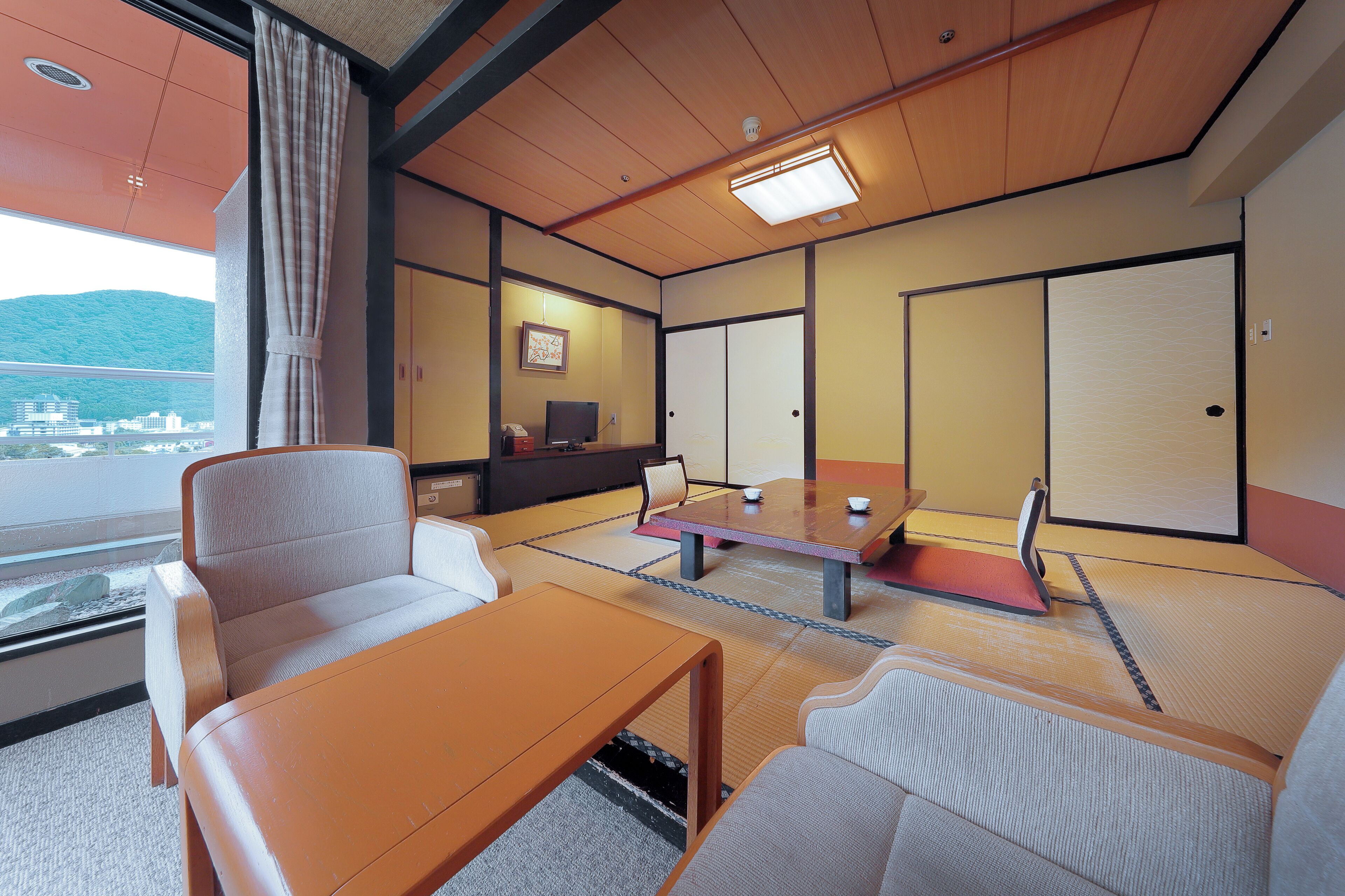 A traditional Japanese room with tatami flooring, a low table, cushioned seating, a television, and sliding doors.