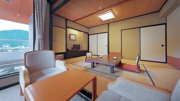 A traditional Japanese room with tatami flooring, a low table, cushioned seating, a television, and sliding doors.