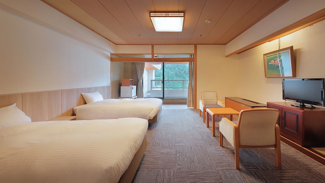 Habitación de hotel con dos camas, un escritorio, una silla, un televisor y una puerta corrediza de vidrio que da a un balcón.