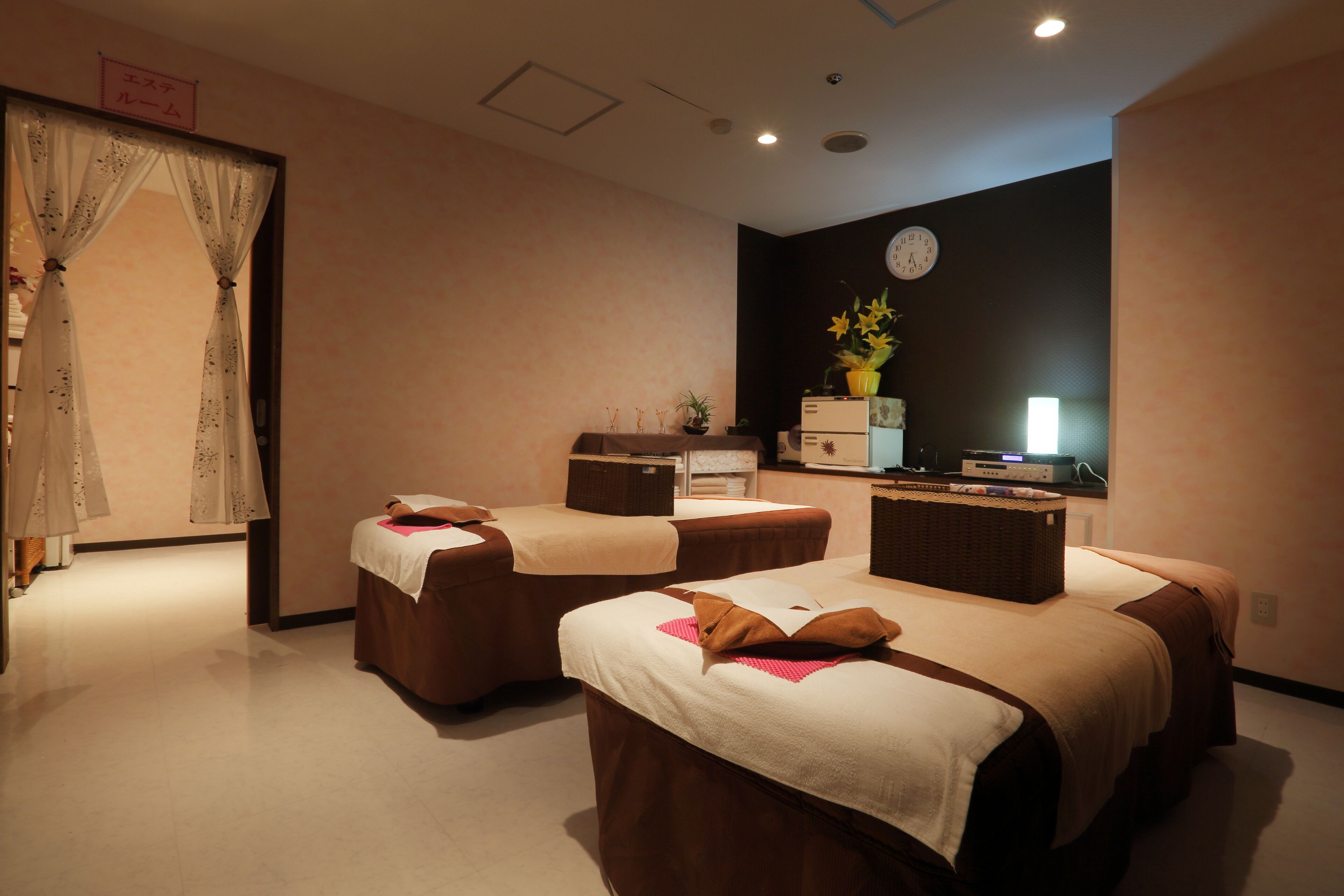 A room with two beds, a desk, a clock, and a potted plant.
