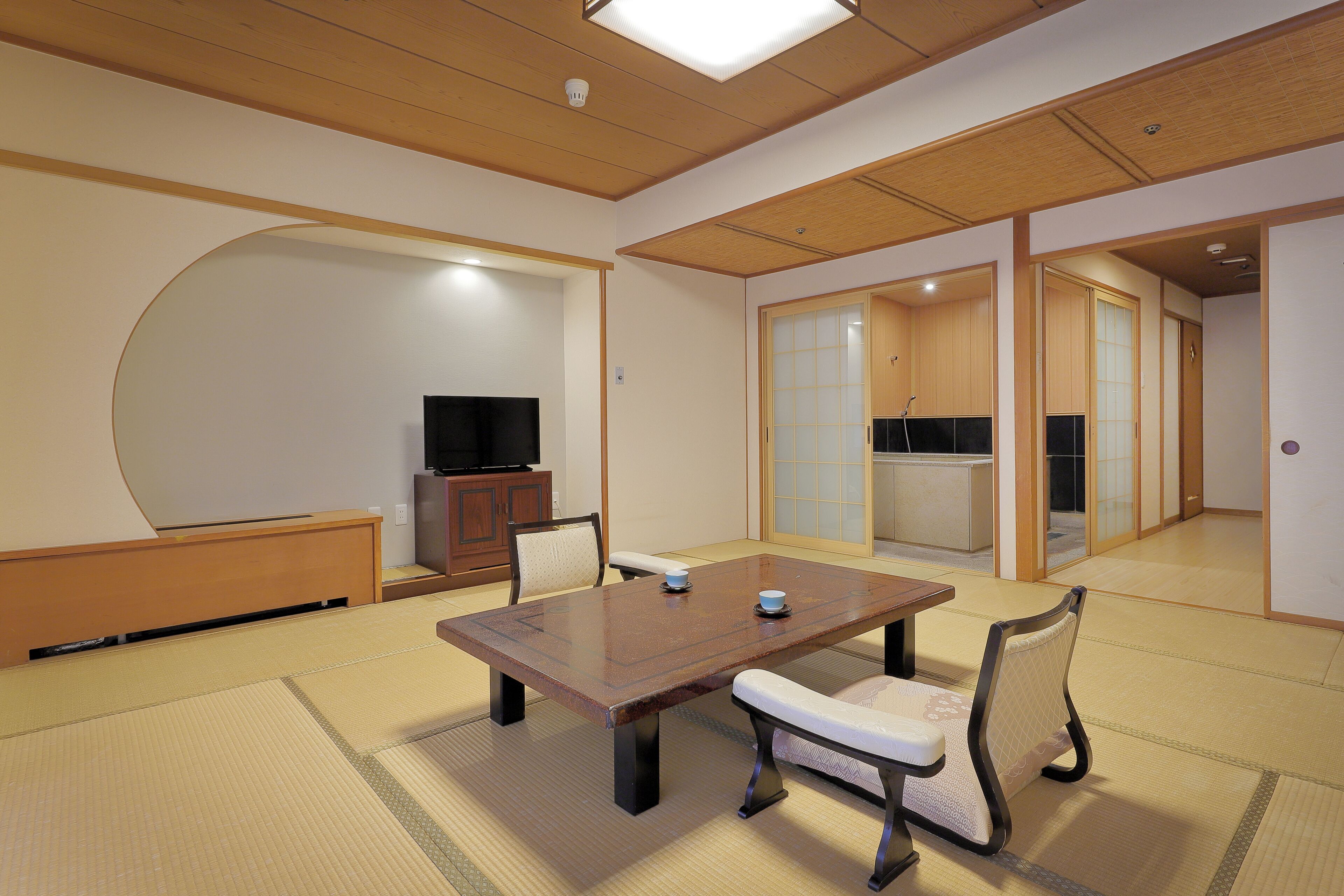 Une pièce de style japonais traditionnel, avec un sol recouvert de tatamis, une petite table en bois et un téléviseur posé au fond.